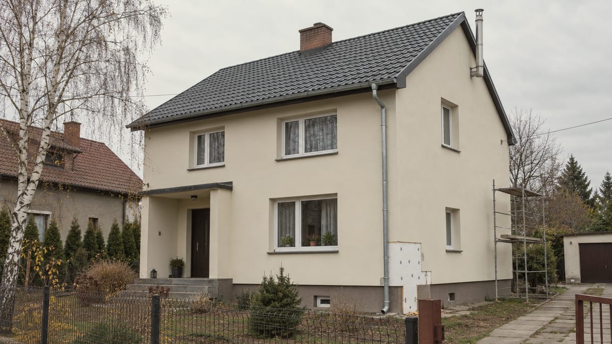 Dom jednorodzinny z nową elewacją i ciemnym dachem, z rusztowaniem przy bocznej ścianie